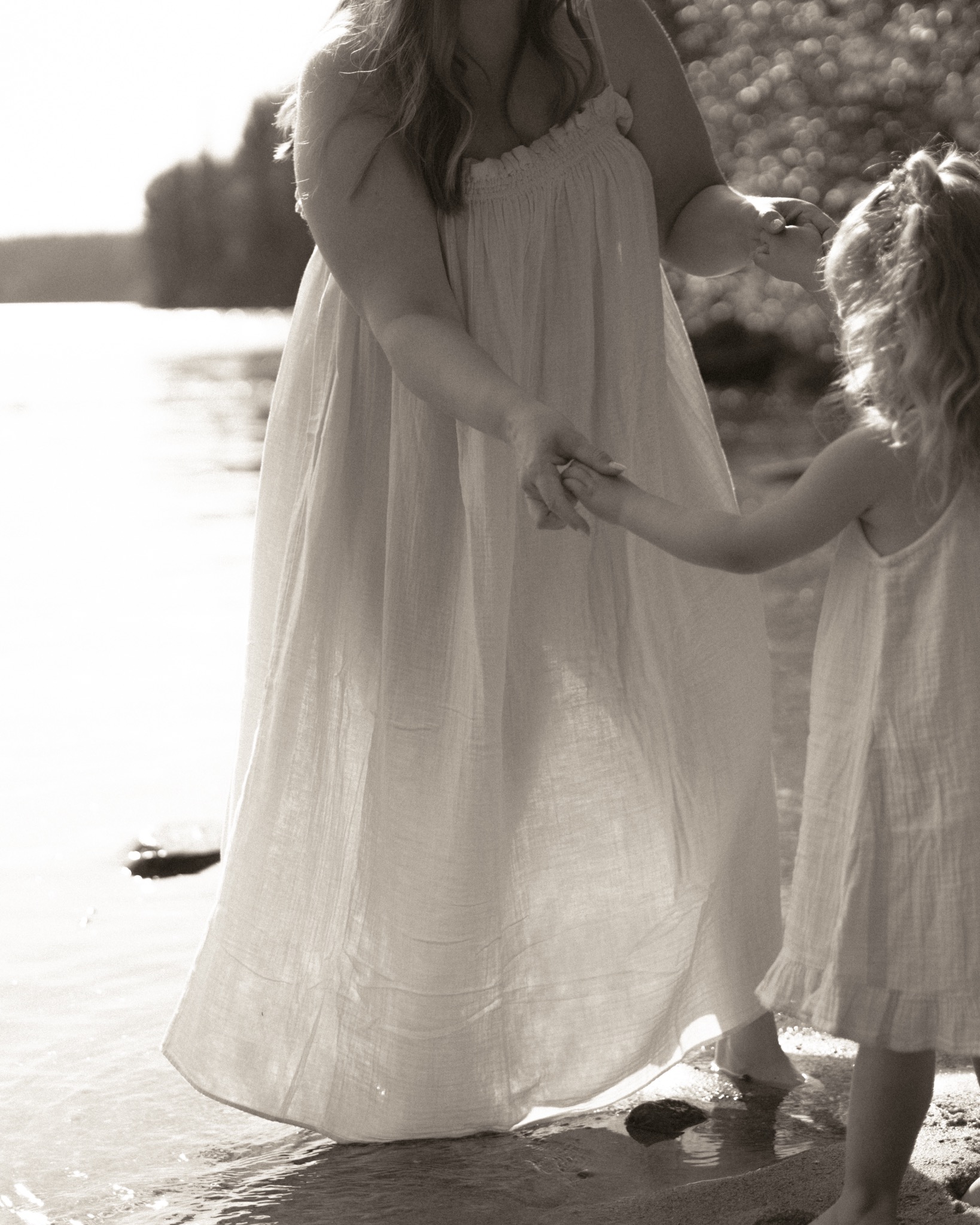 A mother holding her child's hands beside the water