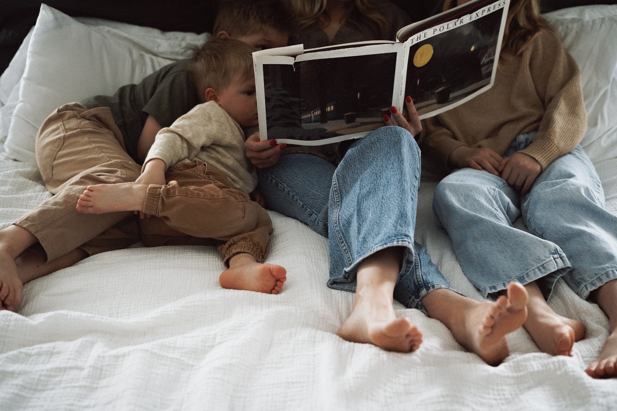 A parent reading with three children in bed