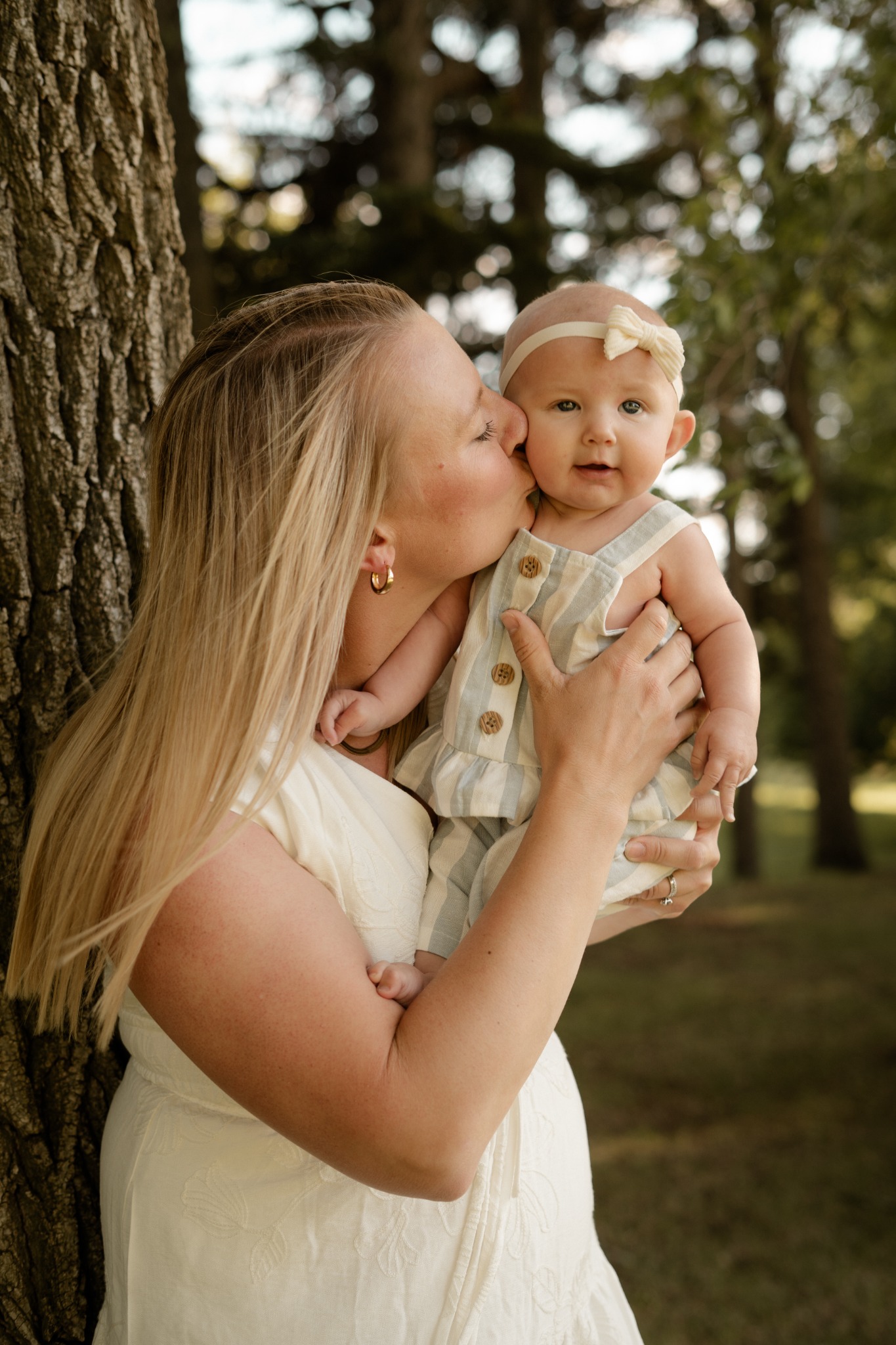 A mother kissing her baby beneath a tree