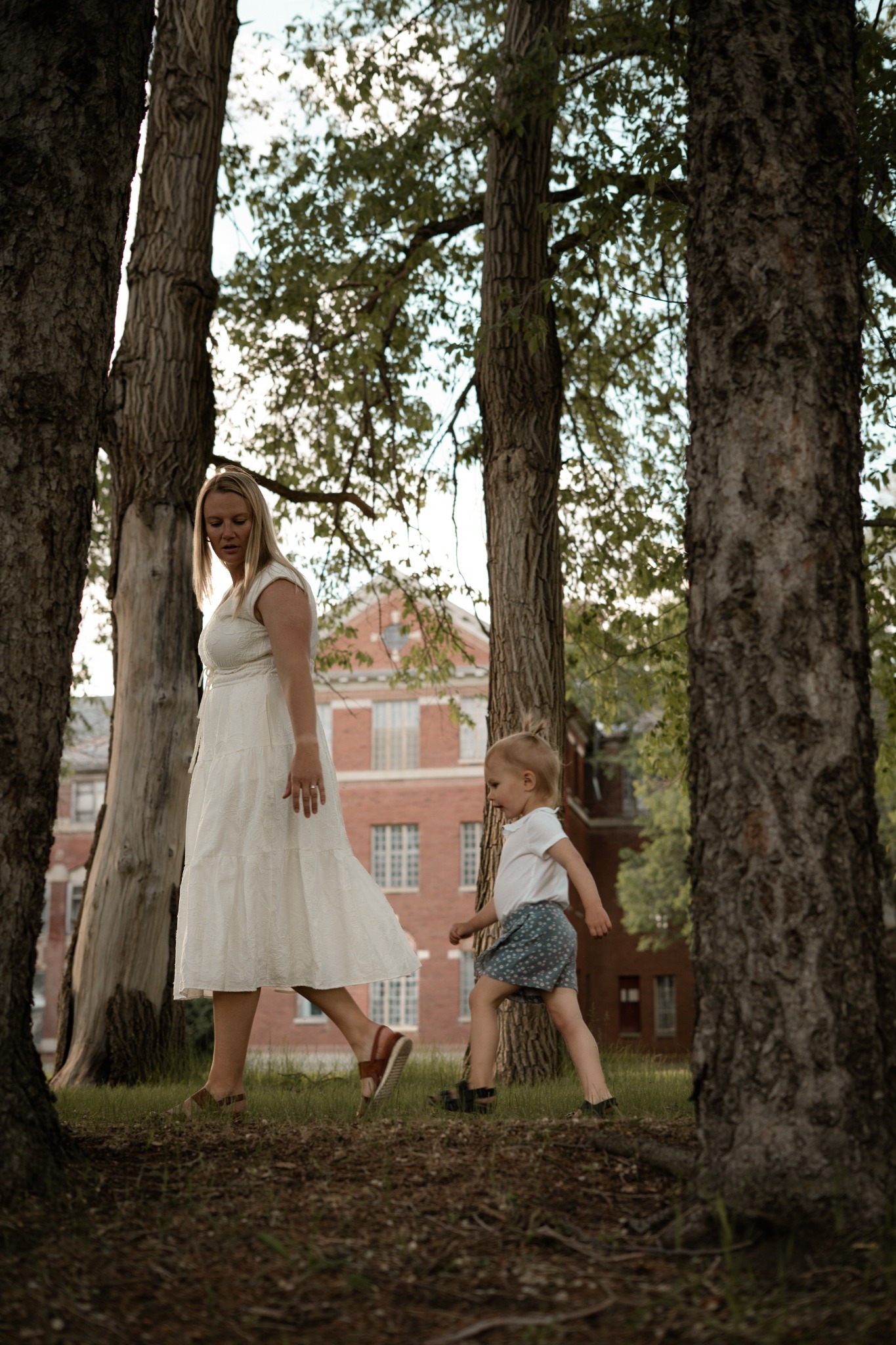 A mother walking beneath trees with her young child